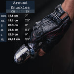 Close-up of a gloved hand gripping a motorcycle handle. A size chart overlays the left, displaying hand measurements in centimeters and inches for sizes XXS to XL, ranging from 17.8 cm to 24.13 cm (7" to 9.5"). The Kaya Movement Custom Dragon Scale Leather Gloves, Fingerless Motorcycle & Driving Gloves are rugged and detailed, perfect for motorcycle enthusiasts with a gothic fashion flair looking for post-apocalyptic and stagewear accessories.