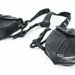 Close-up of a pair of KERO Unisex Lightweight Leather Holster Bags by Kaya Movement, crafted from black sheep skin leather with utility belts and pouches. The belts and pouches showcase detailed stitching and metal snap buttons. The intertwined straps and riveted patches emphasize the sturdy, practical design. Perfect as unisex leather holster bags, they are laid out on a white surface.