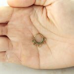 A hand holding the MAWAR Lotus Flower Septum Ring in Gold by Kaya Movement, an 18 gauge gold-colored nose ring with a floral design. Crafted from gold brass body jewelry, the ring features ornate petal-shaped extensions that add to its intricate appearance. The background is blurred, highlighting this delicate piece in the center of the palm.
