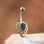 A close-up image showcasing the refined OSALI Marquise Belly Piercing Ring in Gold & Black Pearl by Kaya Movement. This elegant piece displays a gold frame with a Black Mother Pearl center, set on a surgical steel curved barbell and accentuated by a rounded ball at the top end. The soft, muted brown background enhances its luxurious design.