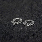 Two MARVDASHT Medium Cyborg Clicker Ear Weights in 925 Silver by Kaya Movement lie on a textured black surface. The ear weights feature a spiral design, resembling intertwined layers or ridges, creating a sophisticated and artistic look against the dark background, reminiscent of silver cyborg earrings from a futuristic world.