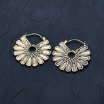 A pair of MOSAIC Ethnic Mandala Disc Hoop Earrings in Gold by Kaya Movement with intricate, fan-like designs radiating from the center, placed against a dark textured background. These boho statement earrings boast a unique geometric pattern that gives them an elegant and artistic look.