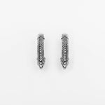 The MARVDASHT Small Biomechanical Clicker Ear Weights in Silver Brass by Kaya Movement are displayed on a white background. These 2-gauge ear weights have an elongated, pointed shape with intricate, layered detailing that creates a textured, feather-like appearance—reminiscent of elegant post-apocalyptic body jewelry.