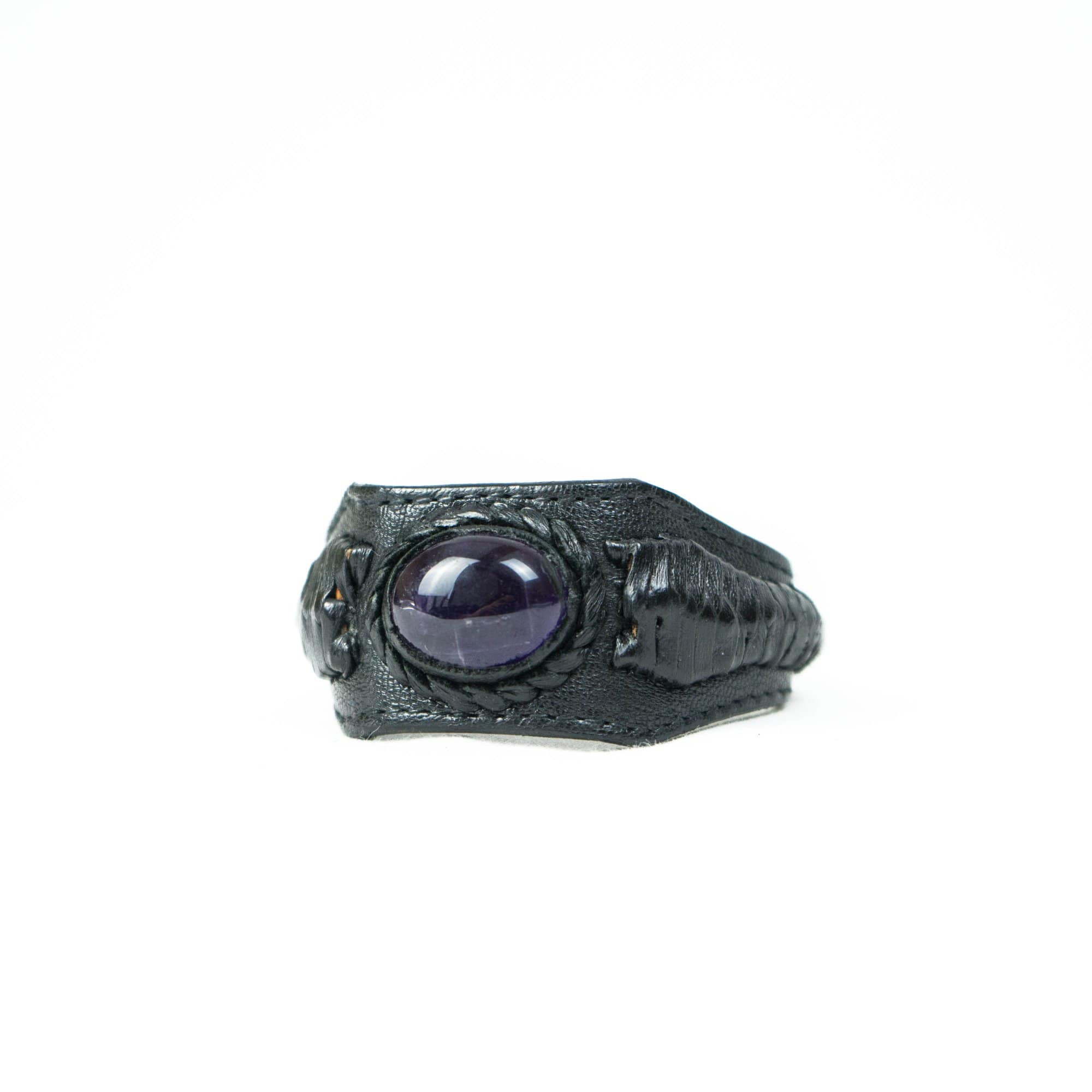 Introducing the Kaya Movement's ANOM Men's Black Cuff Leather Bracelet featuring a polished genuine Amethyst gemstone at its center. The intricately detailed leather band, with a slightly rugged texture, beautifully frames the glossy stone, making it stand out against a plain white background. This piece is reminiscent of an artfully refined black leather bracelet.