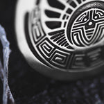 Close-up of the Kaya Movement CROP CIRCLE Oversized Tribal Disc Hoop Earrings in Silver, intricately engraved with geometric patterns including spirals and lines, giving it a boho body jewelry or tribal earrings aesthetic. It is placed on a dark textured background.