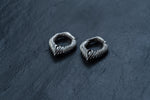 A pair of MARVDASHT Small Biomechanical Clicker Ear Weights in 925 silver, by Kaya Movement, are placed on a dark, textured surface. The 2-gauge ear weights feature an intricately detailed, scaly pattern with pointed ends, evoking a mythical, fantasy-inspired aesthetic with subtle sci-fi vibes.