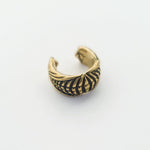 A close-up image of the DARMA Fake Septum Ring or Ear Cuff in Gold by Kaya Movement, showcasing intricate, symmetrical cut-out designs reminiscent of leaves or feathers. The design evokes a blend of natural elegance and avant-garde style, characteristic of post-apocalyptic body jewelry. Set against a plain white background to highlight its details and craftsmanship.