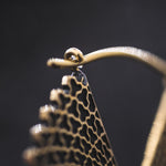 Close-up of a gold VORTEX Tribal Oversized Mandala Disc Hoop Earring by Kaya Movement with an intricate, cut-out design on a black background. The earring features a hook clasp, and the delicate, detailed texture captures the charm of boho statement earrings.
