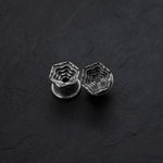 Two HEXA Futuristic Geometry Hexagon Flesh Tunnels from Kaya Movement, featuring intricate, layered designs, are displayed on a dark, textured background. Resembling elegant earrings for stretched ears, these silver hexagonal tunnels exhibit a three-dimensional stair-like pattern inside their shape, giving them a unique architectural appearance. Available in sizes from 12mm to 24mm.