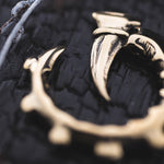 Close-up of the GIGER Biomechanical Open Ended Hoop Ear Weights in Gold by Kaya Movement, set against a dark, textured background. The ear weights feature sharp, curved points and intricate detailing, reminiscent of designs seen in dystopian festivals. Part of a white element is visible on the top left corner of the image.