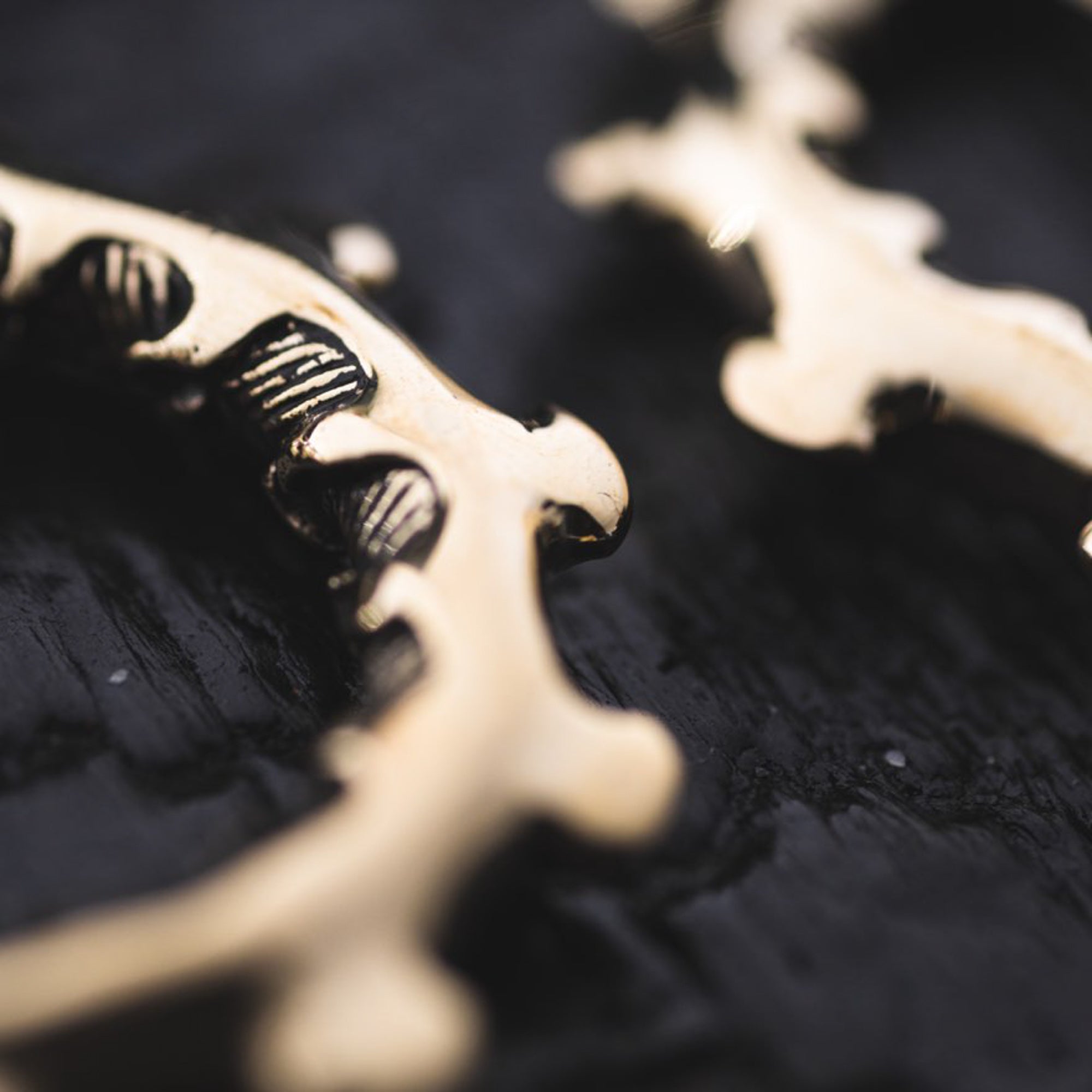 Close-up of the GIGER Biomechanical Open Ended Hoop Ear Weights in Gold by Kaya Movement, lying on a dark surface. The intricate patterns and reflective gold material stand out against the background, suggesting a decorative unisex 0 gauge jewelry piece.