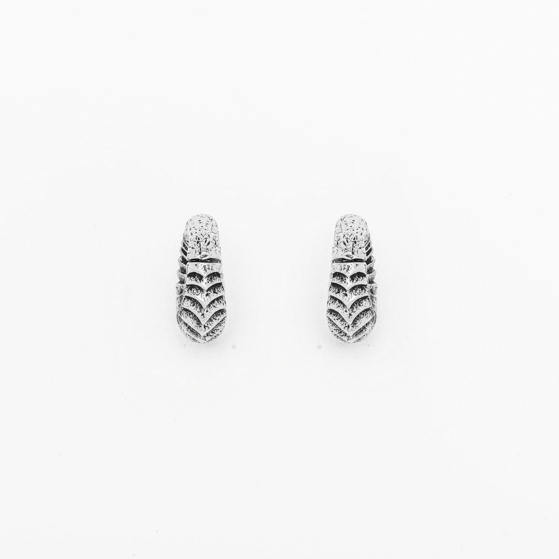 The AARO Cyborg Clicker Hoop Ear or Septum Weights from Kaya Movement are a pair of small, pendant-style earrings made of 925 silver, featuring a textured, scalloped design. Each earring boasts an elongated teardrop shape and intricate detailing that gives them a vintage, artisanal appearance. These 6-gauge weights are perfect for those with stretched ears or as a complement to a septum piercing. The background of the product image is plain white.