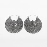 The PANCHA Oversized Tribal Shipibo Disc Earrings in Silver by Kaya Movement feature a pair of large, circular statement earrings with intricate, symmetrical geometric patterns etched into their surfaces. These 16-gauge silver earrings have a hook clasp and are beautifully displayed against a white background.