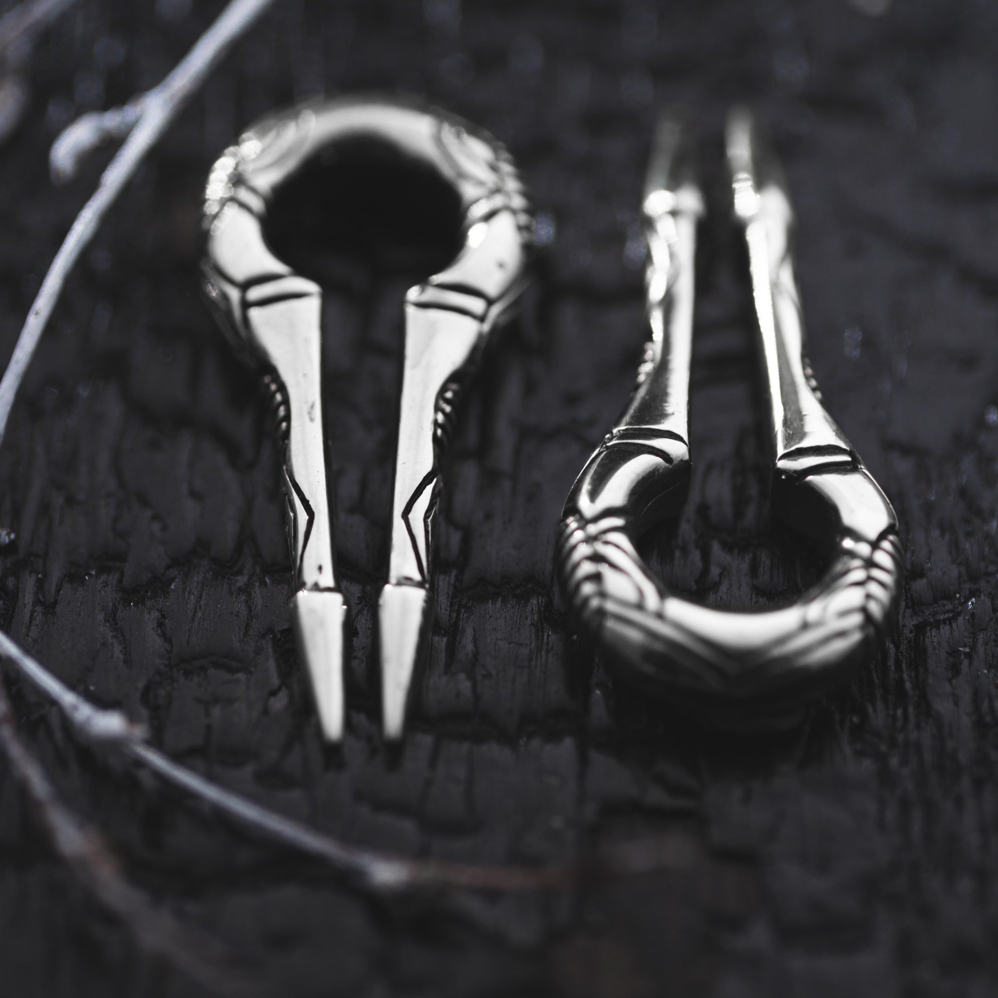 Close-up of two silver EXRO Biomechanical Cyborg Keyhole Ear Weights by Kaya Movement, placed on a dark textured background. The 2 gauge ear weights feature intricate engravings and a looped design, resembling unisex gauge earrings with their polished metallic finish.