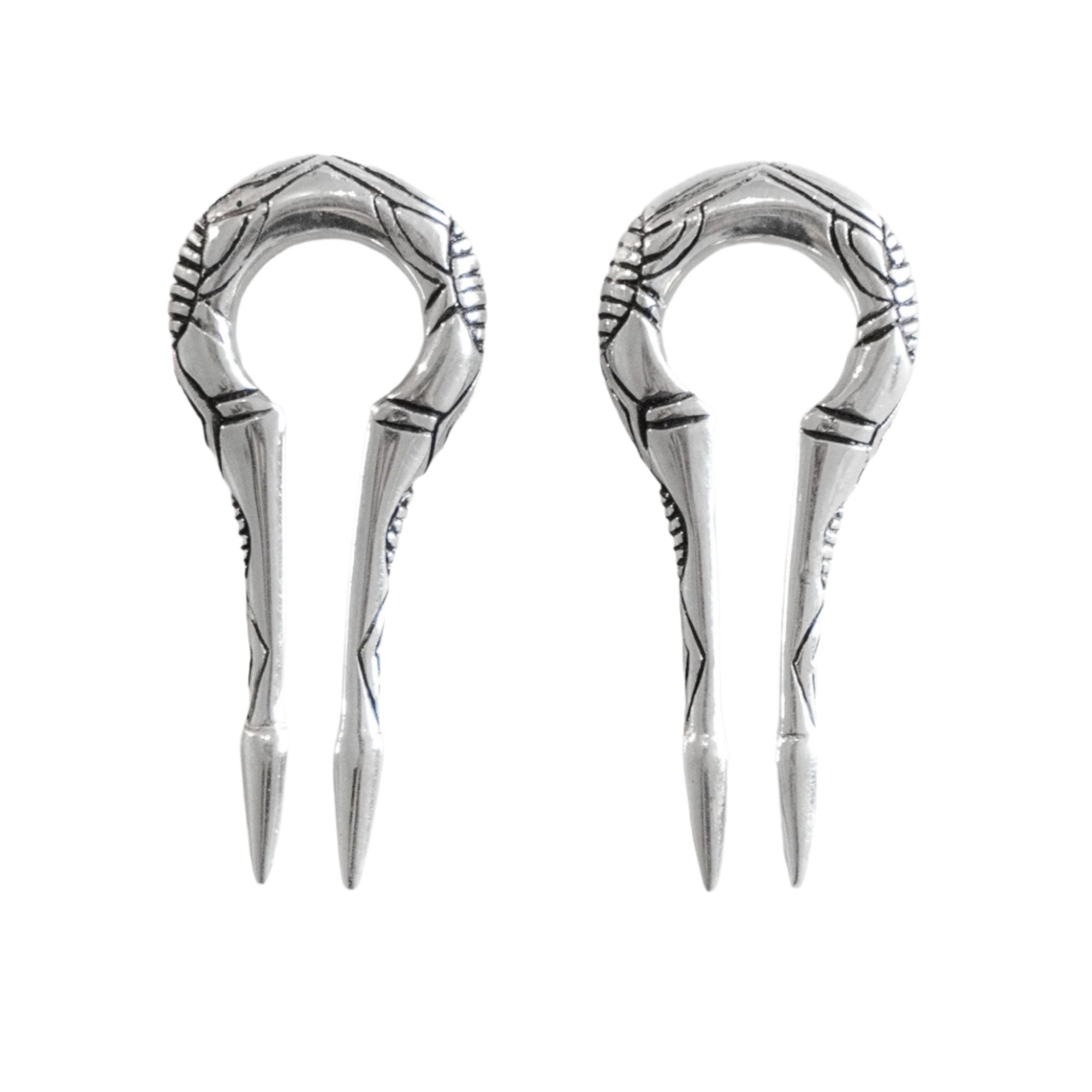 A pair of EXRO Biomechanical Cyborg Keyhole Ear Weights in 925 Silver by Kaya Movement, designed with a circular top and two pointed prongs, echoing the craftsmanship of unisex gauge earrings. The ear weights feature an intricate ornamental pattern and are displayed side by side against a white background.