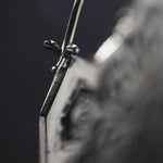 Close-up image of a safety pin fastened through a piece of fabric. The image focuses on the clasp section of the safety pin, reminiscent of the intricate craftsmanship found in Kaya Movement's ASA Oversized Asa No Ha Mandala Disc Earrings in Silver | 16 gauge. The background is dark and out-of-focus, highlighting the metallic texture of the pin.