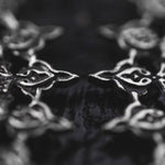 A close-up image of the MOZAIKA Oversized Gothic Disc Earrings in Silver (16 gauge) by Kaya Movement, showcasing intricately detailed metallic patterns with interconnected shapes that resemble stylized flowers or leaves. The dark and glossy background enhances the reflective quality of these exquisitely designed earrings, evoking a sense of gothic elegance.