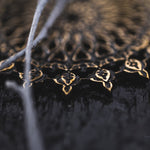 Close-up of a dark circular object with intricate golden patterns, resembling mandala art. Two out-of-focus, light-colored, thread-like elements cross the top left area of the image, creating a soft contrast against the detailed background, reminiscent of Kaya Movement's Mozika Oversized Gothic Disc Earrings in Gold Brass (16 gauge).