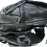 Close-up of the APOPHIS Post-Apocalyptic Leather Shoulder & Belt Bag by Kaya Movement. This black leather bag features a textured, pleated design with metallic snap buttons and a partially open zipper, revealing part of the interior. Fringed tassels and various intricate details enhance its unique style, making it an ideal wasteland festival accessory.