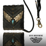 The AMONI Gold Stud Bi-Fold Flip Black Leather Wallet from Kaya Movement features intricate gold detailing and a central labradorite gem. It has a braided leather strap with a metal clasp. The geometric patterns of the Kaya Movement logo are displayed at the bottom right, making it one of their elegant custom leather wallets.