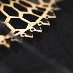 Close-up of the ILLUSION Oversized Cyborg Sci Fi Disc Earrings in Gold by Kaya Movement on a black background. The 14-gauge earrings feature geometric patterns with small circular cut-outs, showcasing fine detailing and craftsmanship reminiscent of post-apocalyptic jewelry.