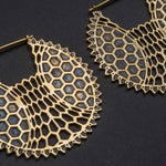 Close-up image of the ILLUSION Oversized Cyborg Sci Fi Disc Earrings in Gold by Kaya Movement on a dark background. These gold earrings feature a visually striking geometric design, combining hexagonal shapes and delicate filigree detailing that evoke a hint of post-apocalyptic jewelry style.