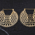 The ILLUSION Oversized Cyborg Sci Fi Disc Earrings in Gold by Kaya Movement are set against a dark background. These 14-gauge earrings feature an intricate hexagonal honeycomb pattern within their circular shape, giving them a delicate yet ornamental appearance that evokes post-apocalyptic jewelry.