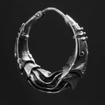 A close-up image of the PROMETHEUS Medium Biomechanical Hoop Earring in 925 silver by Kaya Movement, showcasing its intricate and textured design. The hoop-style earring features overlapping layers and small decorative elements, giving it a rugged, post-apocalyptic body jewelry appearance. The solid, dark background highlights the 18-gauge earring's details beautifully.