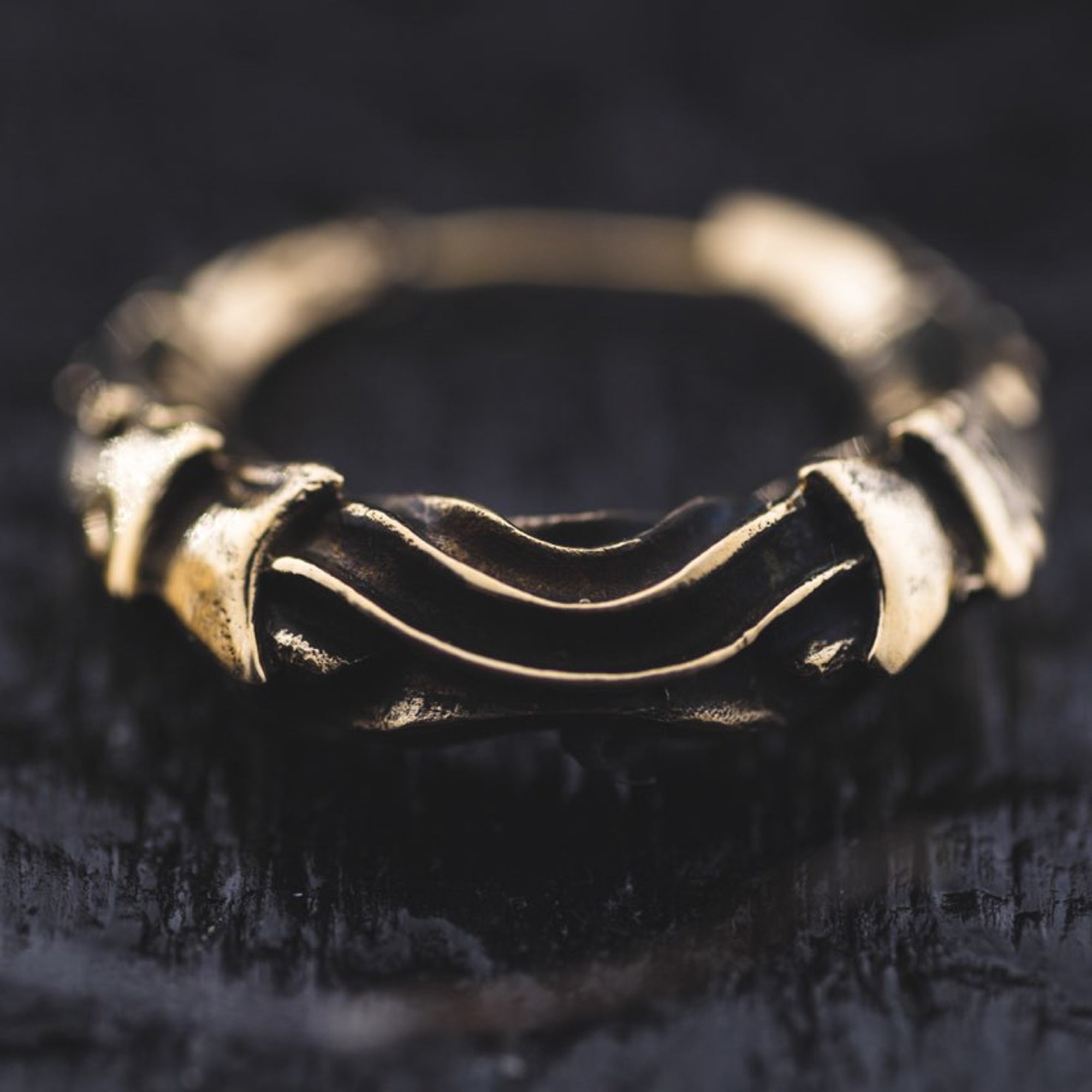 A close-up image of the PROMETHEUS Small Cyborg Hoop Earrings in Gold by Kaya Movement. The earrings feature an intricate, intertwined design and have a worn, rustic appearance reminiscent of post-apocalyptic body jewelry, set against a dark, textured background.