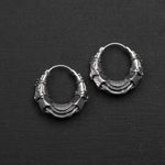 The PROMETHEUS Small Cyborg Hoop Earrings 925 Silver from Kaya Movement, showcased against a black backdrop, are intricately designed with a series of overlapping metal segments. Each earring, crafted in 18-gauge silver, boasts a textured and layered appearance—a true piece of sci-fi statement jewelry.