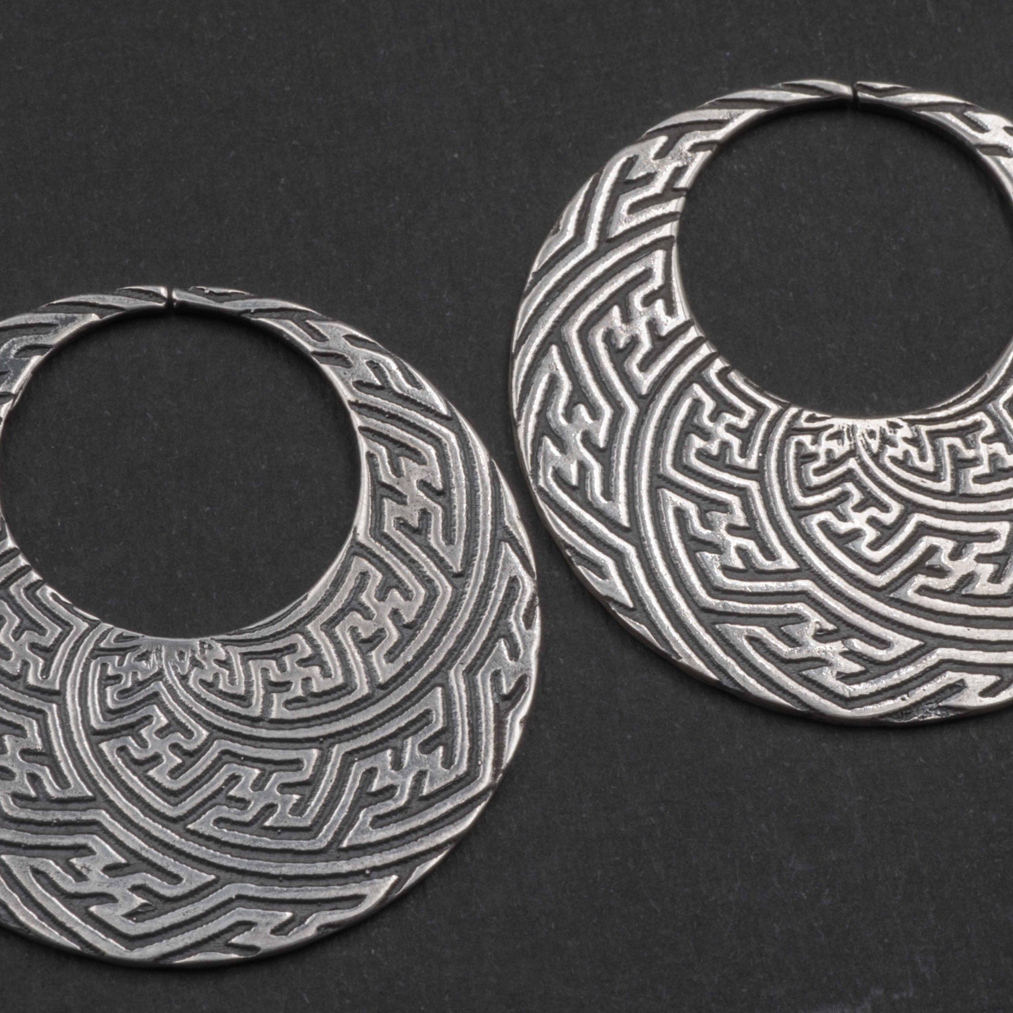 Introducing the SAYAMOON Tribal Sayagata Hoop Disc Earrings by Kaya Movement: crafted in 925 sterling silver, these 12 gauge earrings showcase intricate geometric patterns. Each earring features a flat, open circle adorned with detailed, maze-like designs engraved on a dark background, evoking the essence of tribal body jewelry.
