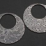 Introducing the SAYAMOON Tribal Sayagata Hoop Disc Earrings by Kaya Movement: crafted in 925 sterling silver, these 12 gauge earrings showcase intricate geometric patterns. Each earring features a flat, open circle adorned with detailed, maze-like designs engraved on a dark background, evoking the essence of tribal body jewelry.