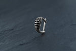 A silver "DIARA Biomechanical Clicker Hoop Septum Nose Ring in Silver | 16 gauge" from Kaya Movement rests on a dark, slate surface. The piece displays smooth curves and detailed engraving that highlight its elegant and intricate craftsmanship—reminiscent of the fine artistry seen in unisex 16 gauge nose piercing designs.