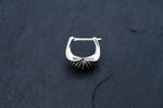The DIARA Biomechanical Clicker Hoop Septum Nose Ring in Silver by Kaya Movement is showcased against a dark, textured background. This 16 gauge earring, with its intricate shell-like design at the base and horseshoe shape complemented by a bar top for fastening, exudes elegance and sophistication.