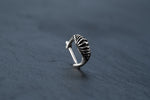 A DIARA Biomechanical Clicker Hoop Septum Nose Ring by Kaya Movement, crafted from 925 silver, rests on a dark, textured surface. The 16-gauge body jewelry features a ribbed, claw-like design with prominent ridges and a curved shape, giving it a distinctive and edgy look.