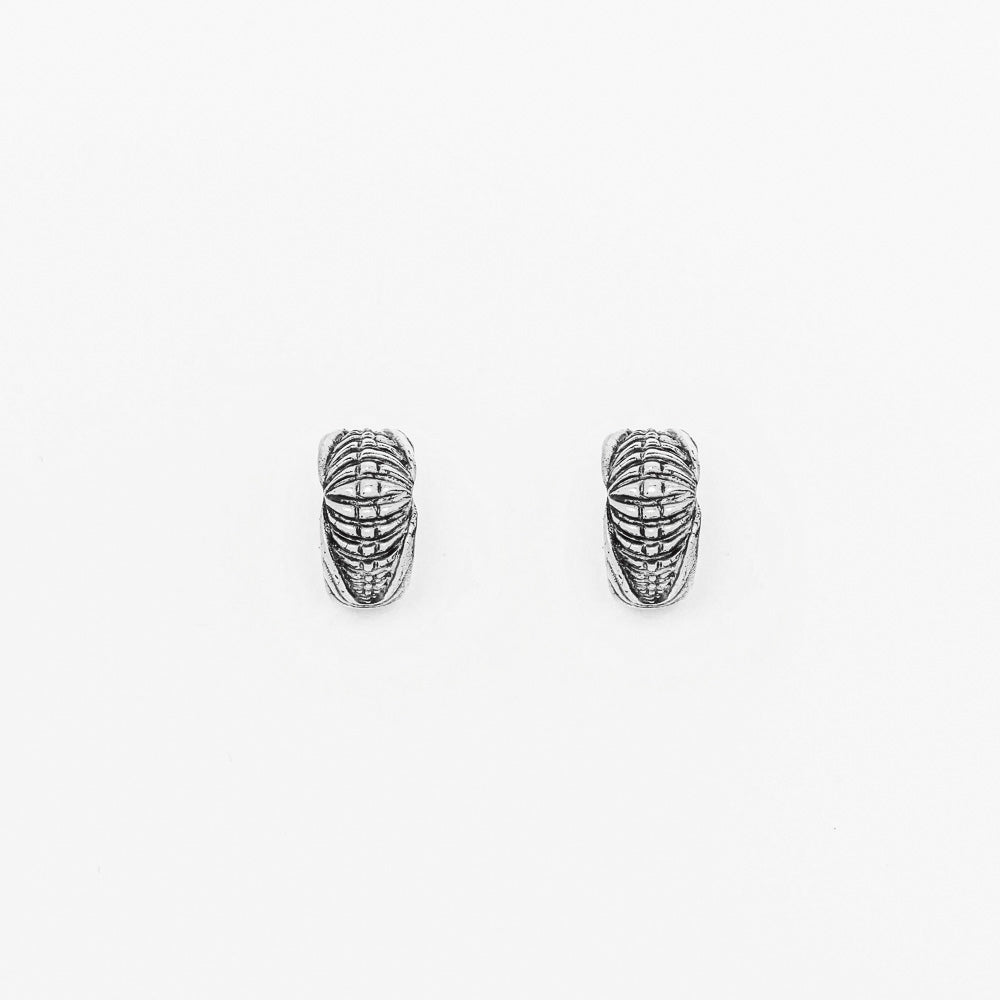 The Darma Biomechanical Clicker Hoop Septum Nose Ring in Silver by Kaya Movement features intricate, etched designs that evoke a post-apocalyptic body jewelry feel. The textured surface showcases horizontal and vertical lines creating a woven pattern. These 16-gauge unisex accessories are displayed side by side on a plain white background.
