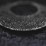 A close-up image of OLIVIA Tribal Shipibo Seamless Disc Hoop Earrings in Silver by Kaya Movement, showcasing their intricate and embossed patterns. The dark and blurred background emphasizes the texture and design of these 12 gauge earrings.