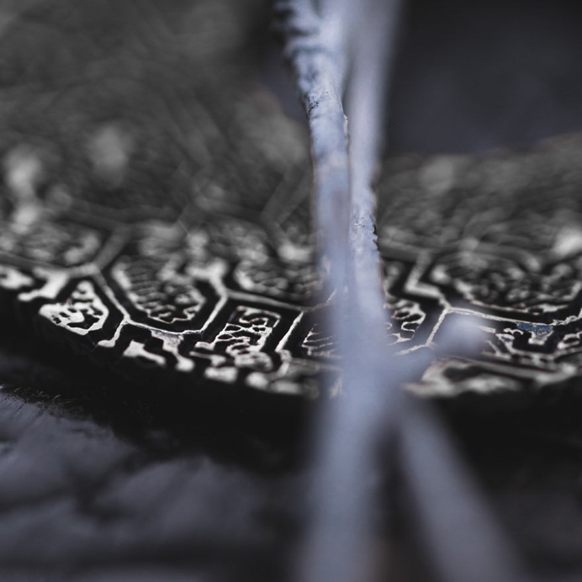 A close-up shot showcases the OLIVIA Tribal Shipibo Seamless Disc Hoop Earrings in Silver by Kaya Movement, highlighting the intricate geometric carvings against a dark, blurred background. The delicate and detailed patterns of these 12 gauge earrings are prominently featured, with a thin, out-of-focus element traversing the image diagonally.
