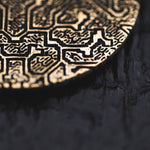 Close-up of a section of the OLIVIA Tribal Shipibo Seamless Disc Hoop Earrings in Gold by Kaya Movement, showcasing its intricate, raised, maze-like patterns. The dark gold color and detailed texture resemble tribal body jewelry. A dark, blurred background accentuates the unique design of this 12-gauge piece.