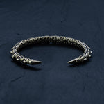 The SHIRO Men's Gold Cuff Bracelet by Kaya Movement features a snake-inspired design with segmented sections and pointed ends. Set against a dark, textured background, the adjustable cuff highlights its intricate detailing and reflective properties.