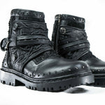 Presenting the MAGMA Wasteland Studded Leather Ankle Combat Boots by Kaya Movement: a pair of black, rugged, leather lace-up punk rock boots featuring textured details, metal studs, straps, and a side zipper. These boots boast intricate stitching and a thick, durable sole designed for heavy-duty wear. The backdrop is plain white.