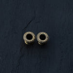 A striking pair of TERA Futuristic Sci Fi Flesh Tunnels in Gold Brass by Kaya Movement, featuring ornate, detailed patterns on a dark, textured surface. These hollow cylindrical objects are available in sizes ranging from 8mm to 20mm and are perfect for body jewelry enthusiasts who appreciate futuristic designs.