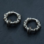 The TRAKARA Heavy Tribal Cyborg Clicker Ear Weights in Silver from Kaya Movement, designed intricately with circular shapes and detailed embellishments, rest on a dark, textured surface. These 2 gauge earrings showcase a vintage, antique aesthetic with ornate patterns and a slightly oxidized finish, reminiscent of tribal cyborg earrings.