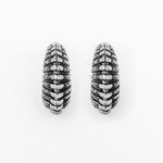 A pair of oxidized TRILOBITE Large Biomechanical Clicker Ear Weights in Silver Brass from Kaya Movement. Resembling post-apocalyptic body jewelry, the 0 gauge ear weights feature a unique pattern of horizontal ridges, creating a ribbed appearance. The edges are slightly darker, accentuating the intricate detailing against a plain white background.