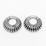 The TRILOBITE Large Biomechanical Clicker Ear Weights in Silver Brass by Kaya Movement are a pair of thick, round earrings with a ridged, textured design that gives them a detailed, ribbed appearance. These 0-gauge post-apocalyptic body jewelry pieces are pictured on a plain, white background.