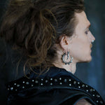 Profile of a person with long, messy hair tied back, wearing a studded black leather jacket and the GIGER Biomechanical Open Ended Hoop Ear Weights in Silver 925 from Kaya Movement. They have a nose piercing and their face is turned to the right, showing a calm expression against a dark background.