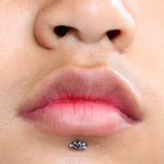 Close-up of a person's lips and nose. The person has a Kaya Movement 925 silver LOTUS Labret Stud body jewelry lip piercing in the center just below the bottom lip, shaped like a lotus flower. The lips are slightly parted, and the skin has a natural and smooth texture.