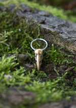 A CROW SKULL Gothic Silver Ring with a Gold Charm by Kaya Movement is placed on a patch of green moss-covered bark. The detailed craftsmanship of the skull and the natural setting with moss and wood textures create a striking contrast, showcasing the allure of handcrafted jewelry.