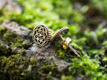 A close-up of the ELLY Flower of Life Stud Earrings in Gold by Kaya Movement, intricately crafted from yellow brass with a geometric pattern, laying on a moss-covered surface. The image highlights the detailed craftsmanship and design of these 18 gauge earrings against the natural, lush green background.