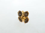 A pair of 18g gauge, gold-colored OM Chakra stud earrings by Kaya Movement with intricate black and gold floral designs, placed on a reflective surface. The reflection creates a symmetrical appearance, enhancing the elegance. These yellow brass earrings come in elegant packaging, making them perfect for gifting.